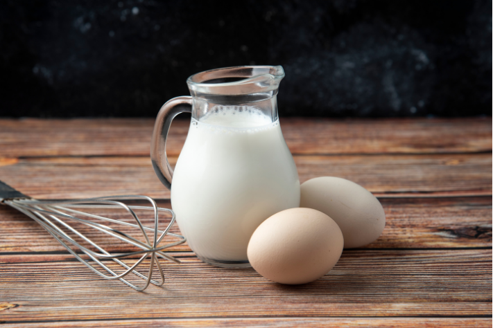 Glass jug of milk with eggs on a wooden surface